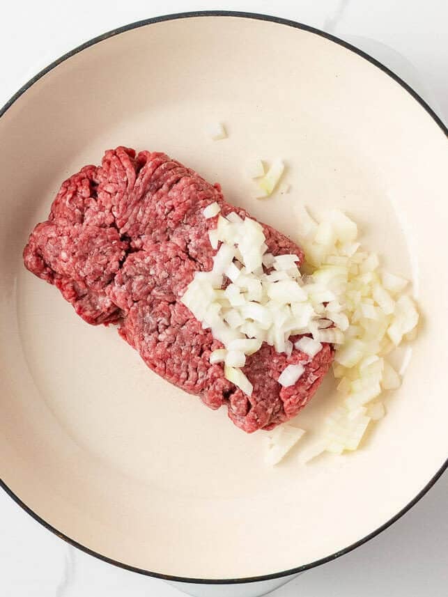 Bite into simpler times with old-school open faced pizza burgers made with seasoned ground beef on a toasted bun, smothered in tomato sauce, melty cheese, and pepperoni! Ground beef and chopped onion cooking in a skillet as the base for pizza burgers.
