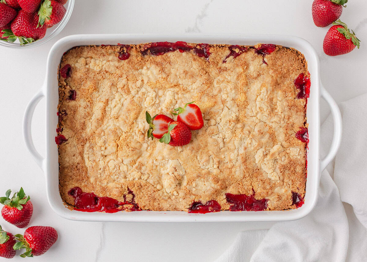 Easy and sweet strawberry cheesecake dump cake is made with strawberry pie filling, cream cheese, boxed cake mix, and just 5 minutes of prep time! Strawberry cheesecake dump cake baked in white 9x13 dish with golden topping and bubbling strawberry edges.
