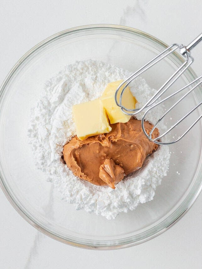 If you love Take 5 candy bars, you are going to love this easy homemade version. No baking required and every bite is the perfect mix of salty, sweet, and crunchy. A glass mixing bowl with crunchy peanut butter, softened butter, and powdered sugar before mixing, with a hand mixer inserted and ready to blend.