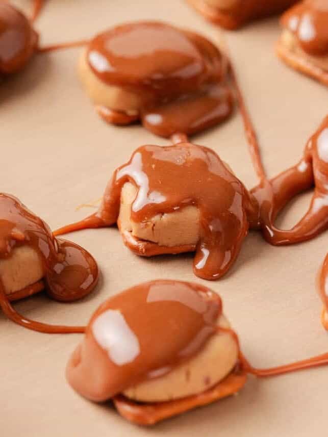If you love Take 5 candy bars, you are going to love this easy homemade version. No baking required and every bite is the perfect mix of salty, sweet, and crunchy. Process shot of peanut butter balls sandwiched between pretzels on parchment, covered in drizzled melted caramel that is spreading and pooling around each piece.