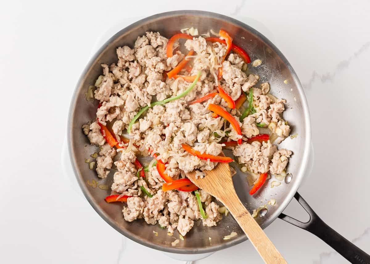 This easy Thai basil chicken recipe is bold, savory, and ready in under 30 minutes. It's everything you love about your favorite Thai food, made right at home! Ground chicken cooking with sliced peppers, garlic, and shallots for Thai basil chicken.