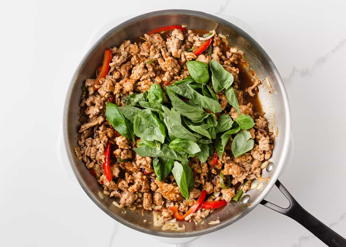 This easy Thai basil chicken recipe is bold, savory, and ready in under 30 minutes. It's everything you love about your favorite Thai food, made right at home! Fresh basil added to Thai basil chicken in skillet before serving.