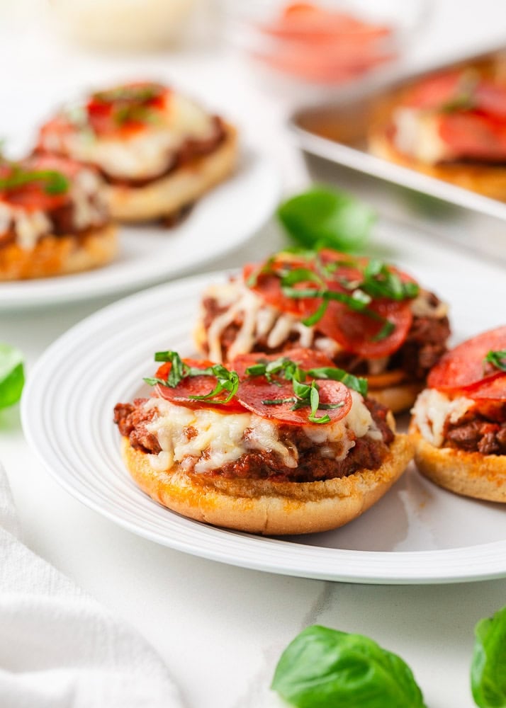 Bite into simpler times with old-school open faced pizza burgers made with seasoned ground beef on a toasted bun, smothered in tomato sauce, melty cheese, and pepperoni! Open-faced pizza burgers on toasted buns topped with seasoned ground beef, melted mozzarella, pepperoni, and fresh basil.