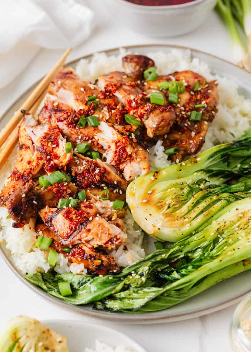 Asian chicken thighs served over white rice with grilled bok choy, green onions, sesame seeds and chili crunch.