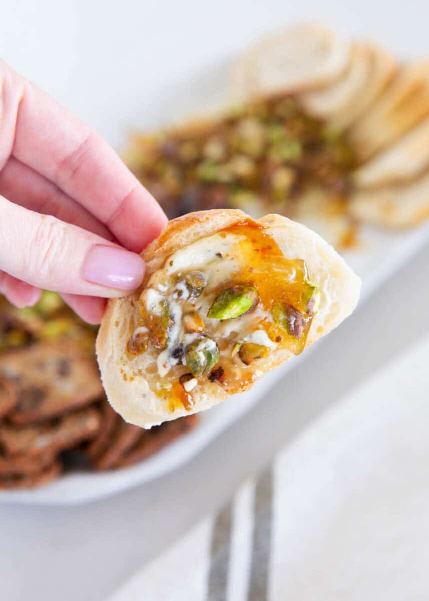 Hand dipping bread into Boursin fig dip with pistachios, fig jam and hot honey.