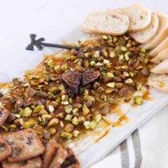 Boursin fig dip with pistachios and hot honey served on a platter with sliced baguette and crackers for dipping.