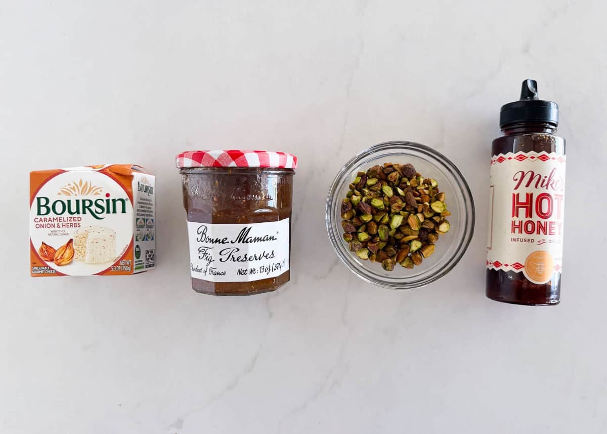 Ingredients for Boursin cheese fig dip including Boursin cheese, fig jam, pistachios and hot honey.