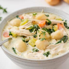 Bowl of creamy chicken gnocchi soup with spinach, carrots, celery and fresh thyme.