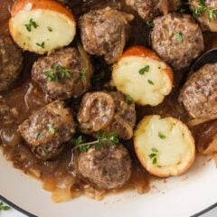 Overhead view of French onion meatballs with caramelized onions, gravy and melted cheese toasts.