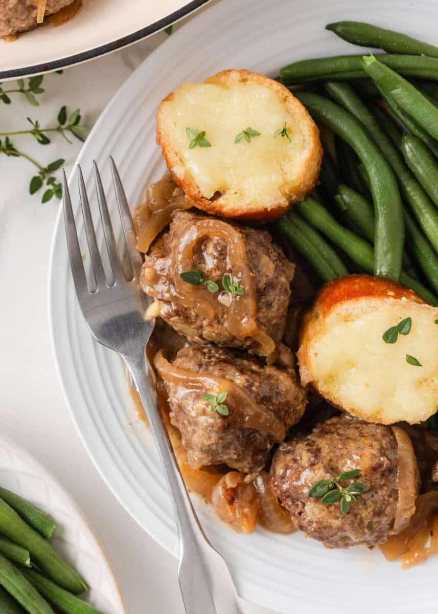 Plate of French onion meatballs with green beans, onion gravy and cheesy baguette slices.