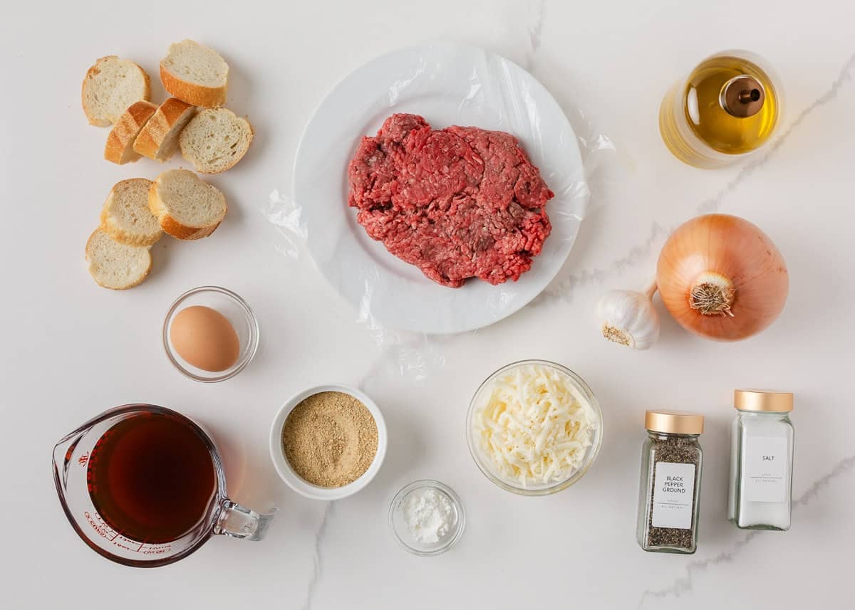 Ingredients for French onion meatballs including ground beef, breadcrumbs, egg, beef broth, onion, garlic, cheese and baguette slices.