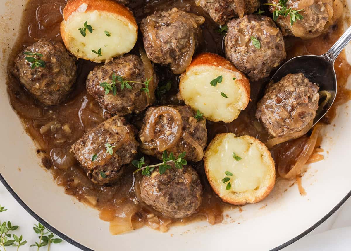 Overhead view of French onion meatballs with caramelized onions, gravy and melted cheese toasts.