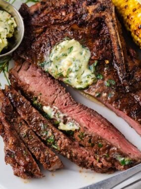 Sliced grilled steak with garlic herb butter melting over the top and grilled corn on the side.