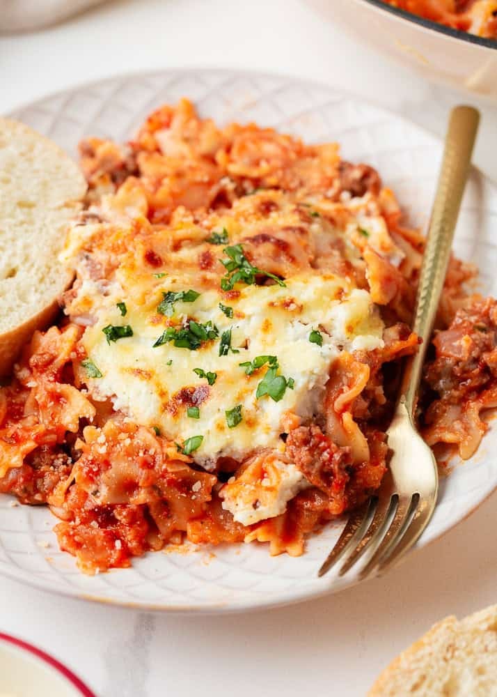 This easy one-pan skillet lasagna comes together on the stovetop in under an hour, with the same bubbly, saucy, cheesy comfort of the classic baked version. Serving of skillet lasagna with cheesy pasta, Italian sausage, and marinara sauce on a plate with bread on the side.