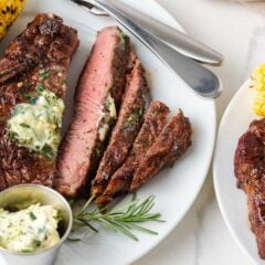 Grilled steak sliced on a white plate with herb butter, rosemary and corn for serving.