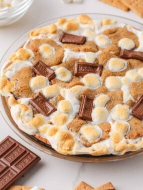 Close-up of baked s&rsquo;mores pie topped with toasted mini marshmallows, graham cracker cookie pieces, and Hershey chocolate squares.