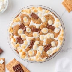 Overhead view of easy s’mores pie with toasted marshmallows, chocolate pieces, and graham crackers on a marble counter.