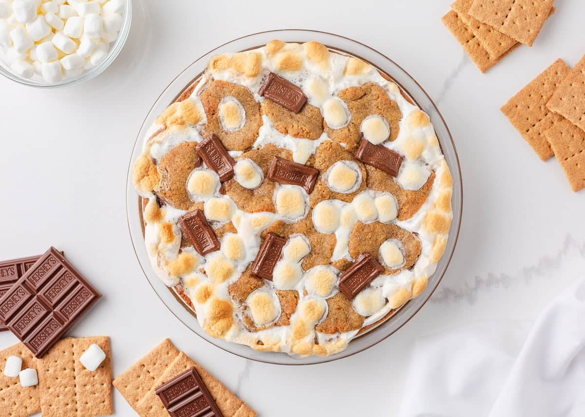 Overhead view of easy s’mores pie with toasted marshmallows, chocolate pieces, and graham crackers on a marble counter.