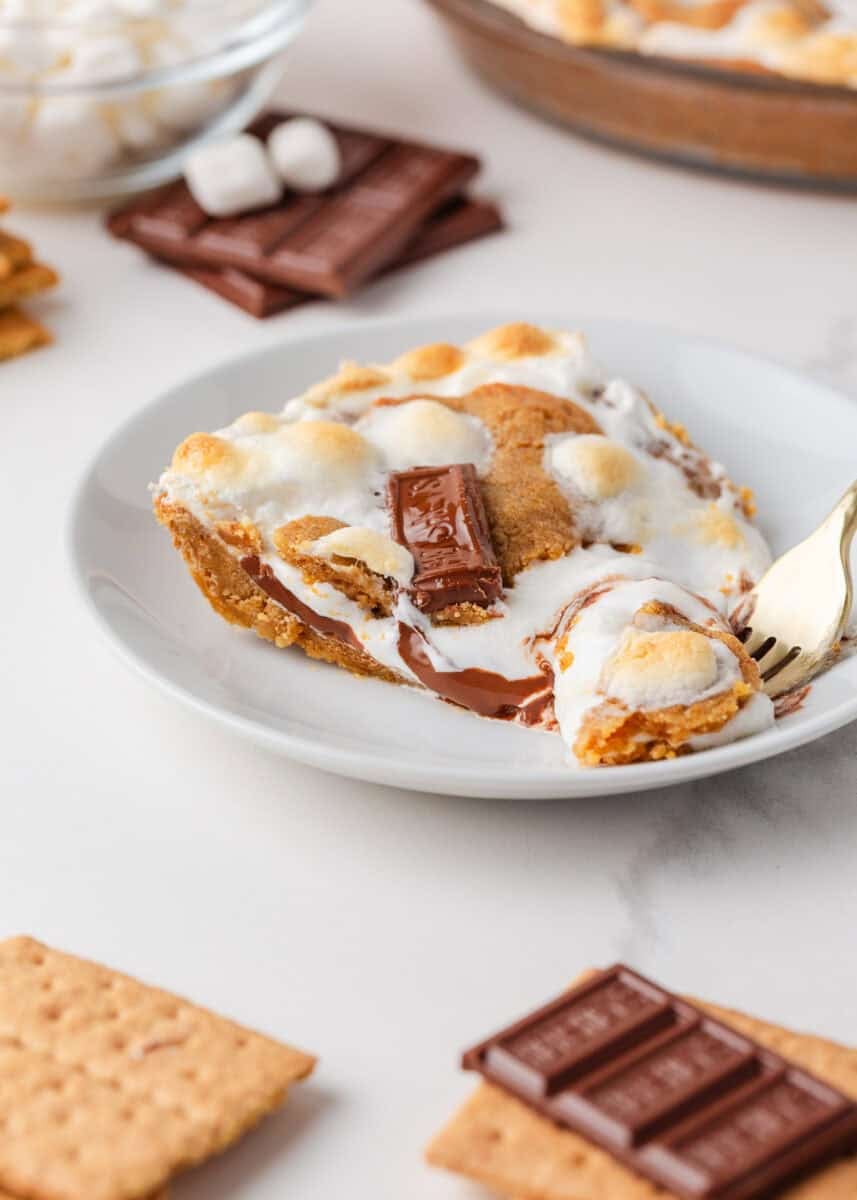 Slice of s’mores pie on a plate with melted chocolate, gooey marshmallow, and golden graham cracker crust.