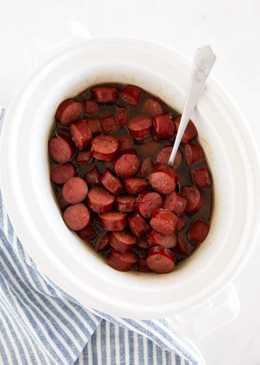 Slow cooker kielbasa bites in a sticky brown sugar glaze with a serving spoon.