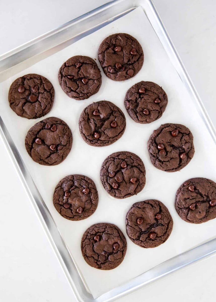 Chocolate cake mix cookies with chocolate chips cooling on a parchment-lined baking pan.