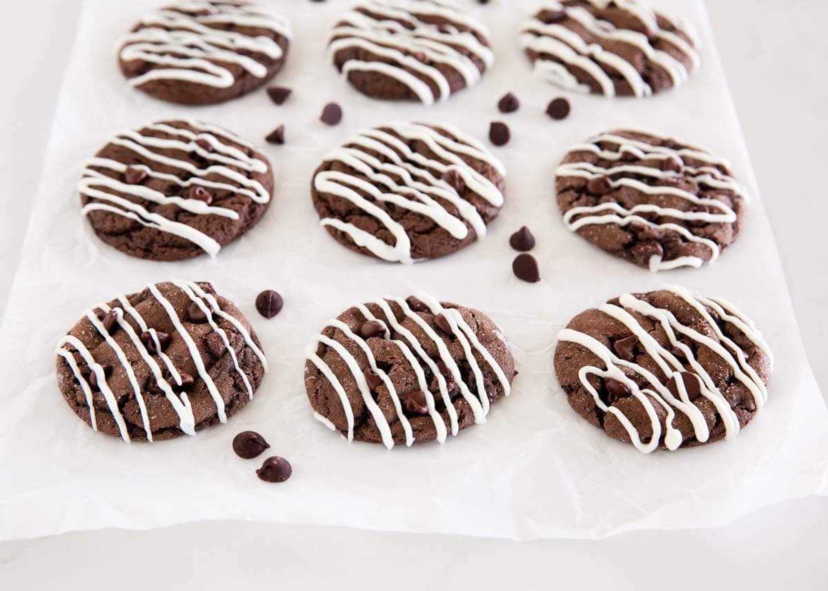 Chocolate cake mix cookies topped with a white chocolate drizzle and chocolate chips on parchment paper.