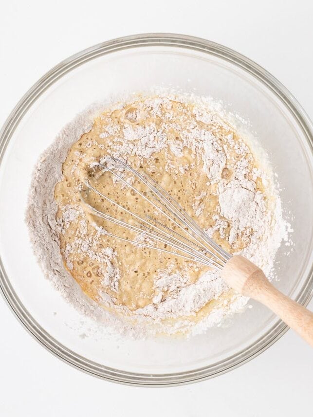 Funnel cake batter being whisked together in a glass bowl as the dry ingredients combine with the wet.