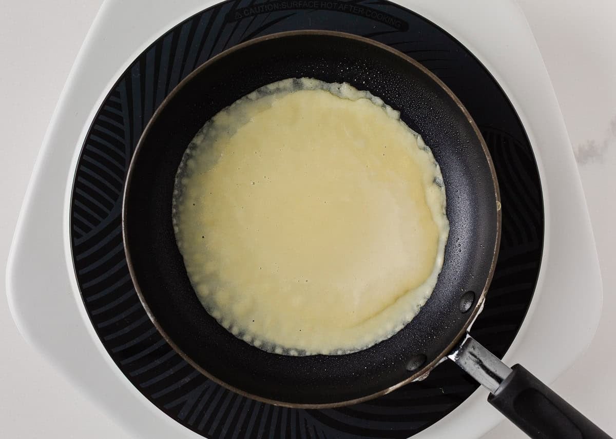 Thin crepe batter spreading in a nonstick skillet.