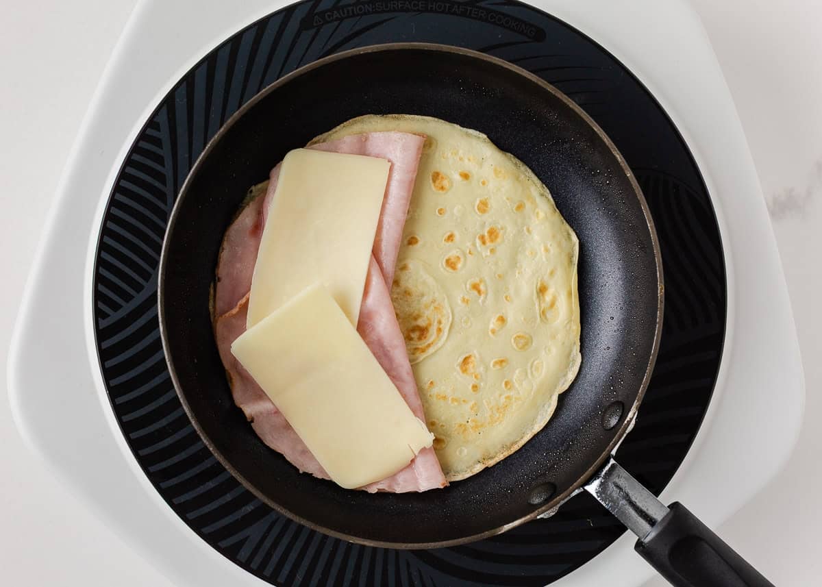Ham and cheese crepe filling cooking in a nonstick skillet.