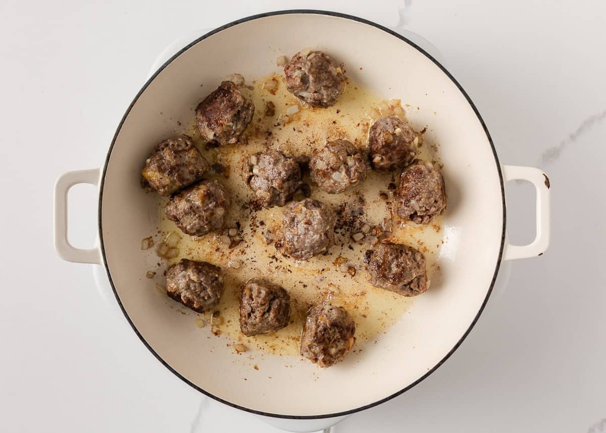 Browned beef meatballs cooking in a skillet for French onion meatballs.