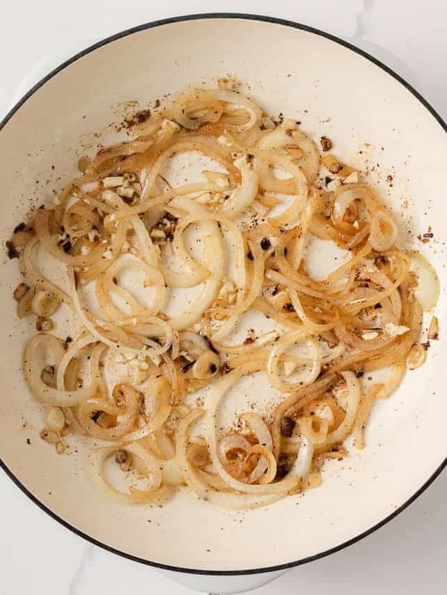 Sliced onions and garlic sautéing until caramelized in a skillet for French onion meatball sauce.