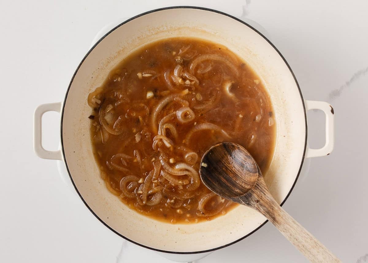 French onion gravy with sliced onions and garlic simmering in a skillet.