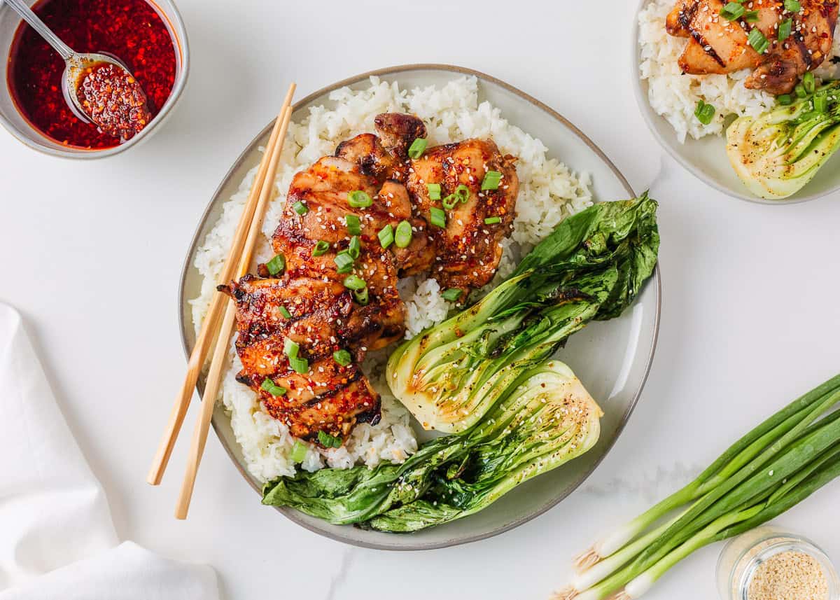 Grilled Asian chicken thighs and bok choy served over fluffy white rice with green onions and sesame seeds.