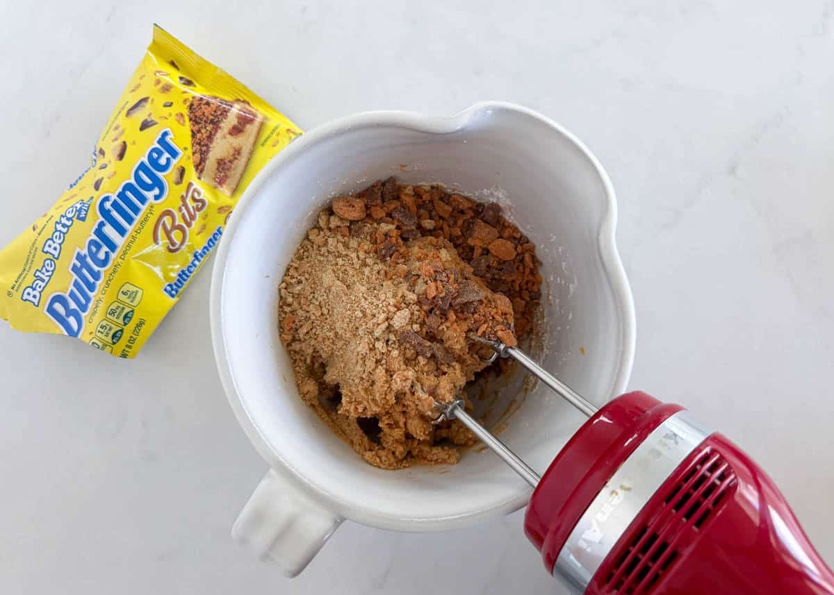 These Butterfinger balls are bite-sized no-bake truffles with crushed Butterfinger candy and graham crackers folded into the filling, then dipped in chocolate. An irresistible sweet treat! Showing how to make butterfinger balls by combining peanut butter, butter and powdered sugar with an electric mixer.