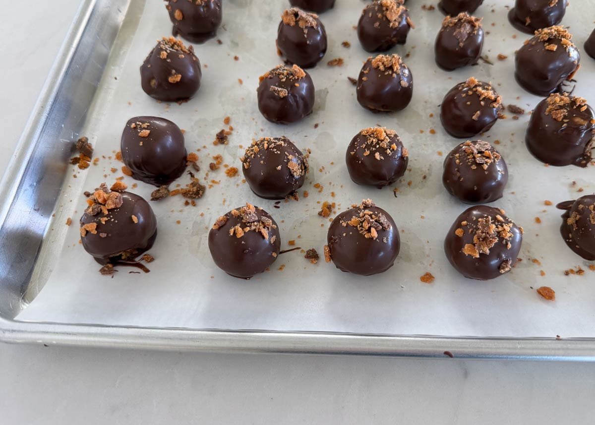 These Butterfinger balls are bite-sized no-bake truffles with crushed Butterfinger candy and graham crackers folded into the filling, then dipped in chocolate. An irresistible sweet treat! Dipped butterfinger balls on parchment paper.