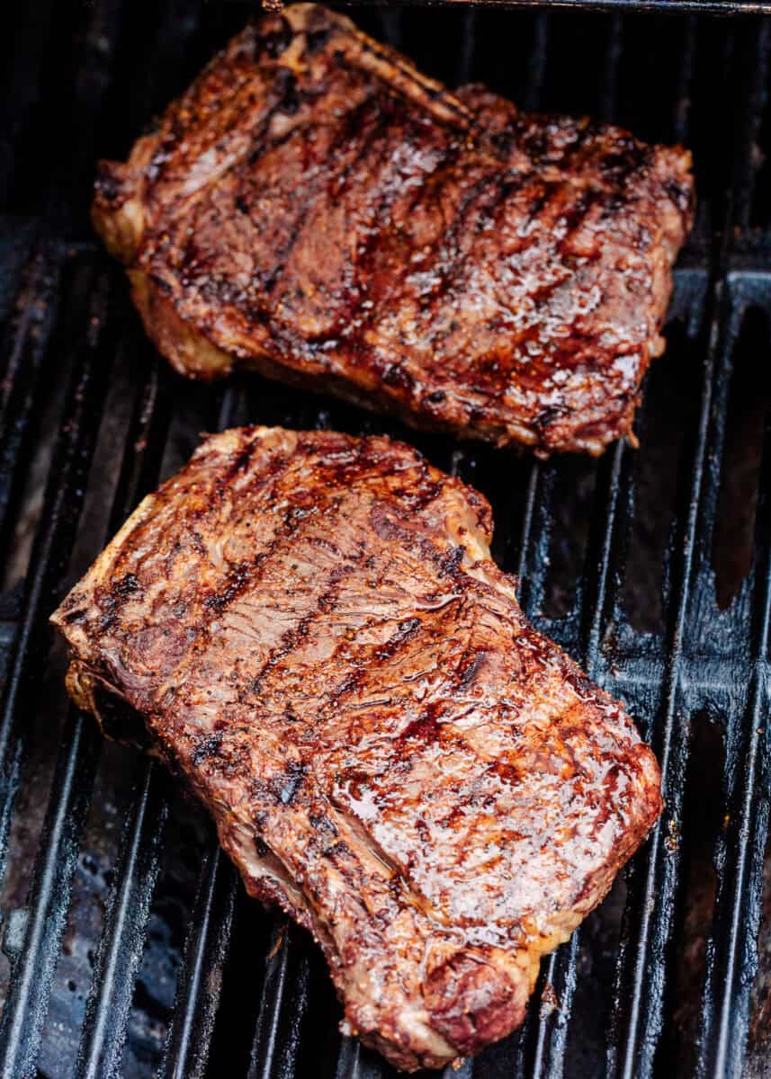 Two grilled steaks searing on grill grates until browned and juicy.
