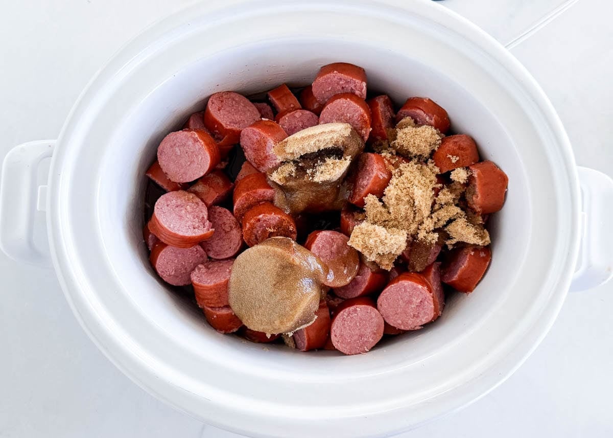 Sliced kielbasa, brown sugar, cola and chili powder added to a slow cooker.