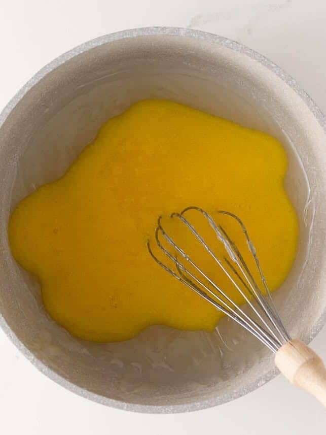 Lemon pie filling thickening in a saucepan with a whisk.