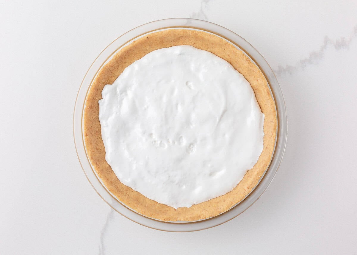 Graham cracker cookie crust pressed into a glass pie dish and filled with marshmallow creme for s’mores pie.