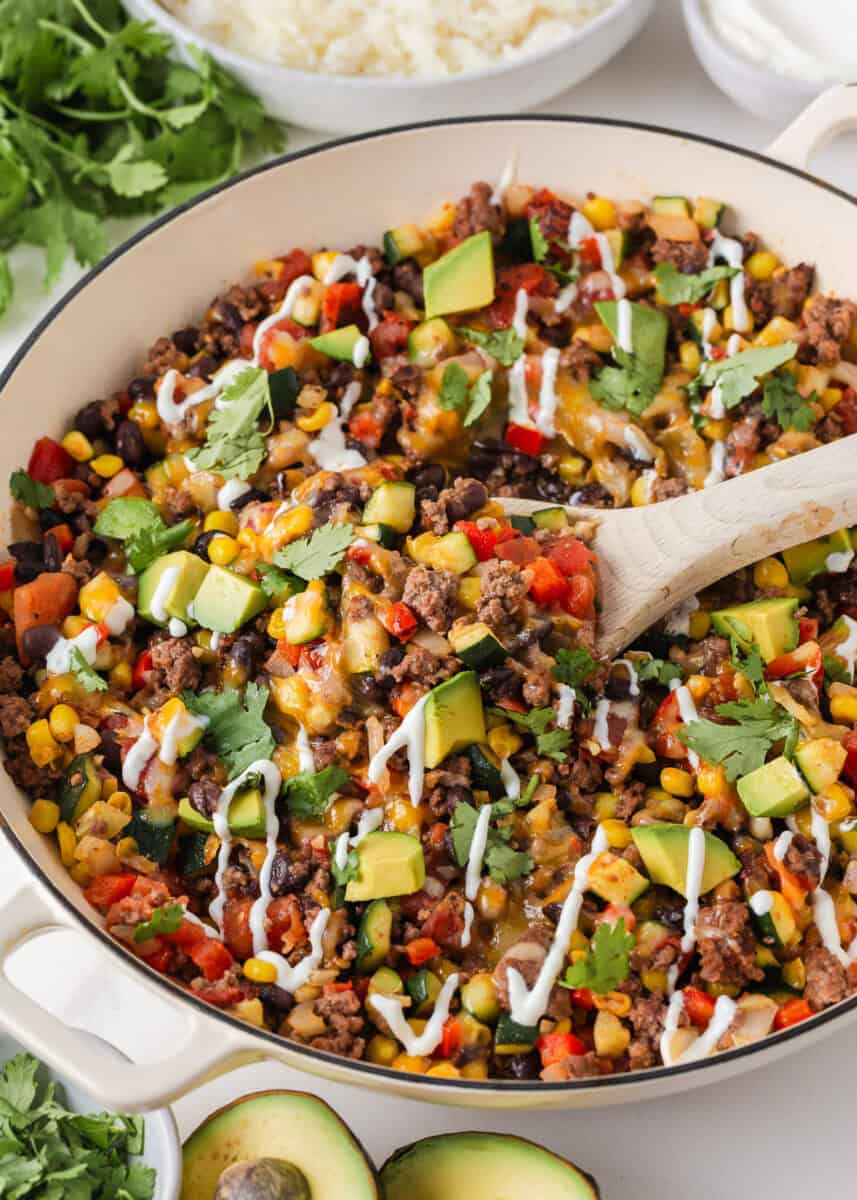 Close-up of a cheesy ground beef and zucchini skillet with black beans, corn, tomatoes, avocado and cilantro.