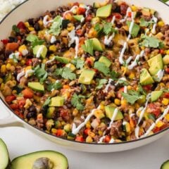 Ground beef and zucchini skillet recipe served in a large pan with avocado, cilantro and sour cream on top.