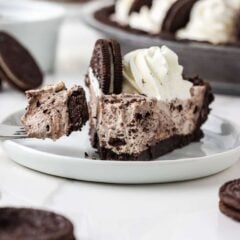 Slice of no bake Oreo cheesecake on a plate with whipped cream and a halved Oreo, with a bite on a fork.