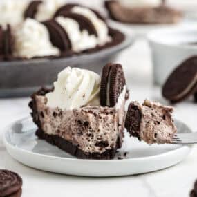 Bite of no bake Oreo cheesecake on a fork next to a slice showing the creamy Oreo filling and cookie crust.