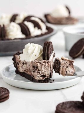 Bite of no bake Oreo cheesecake on a fork next to a slice showing the creamy Oreo filling and cookie crust.