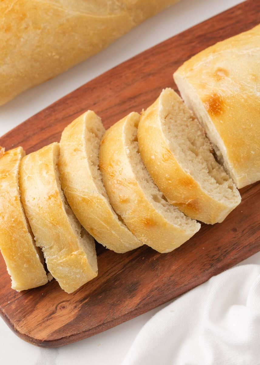 Sliced sourdough French bread on a wooden board showing the soft inside and golden crust.
