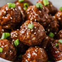 Glossy sticky pork meatballs topped with sesame seeds and sliced green onions.
