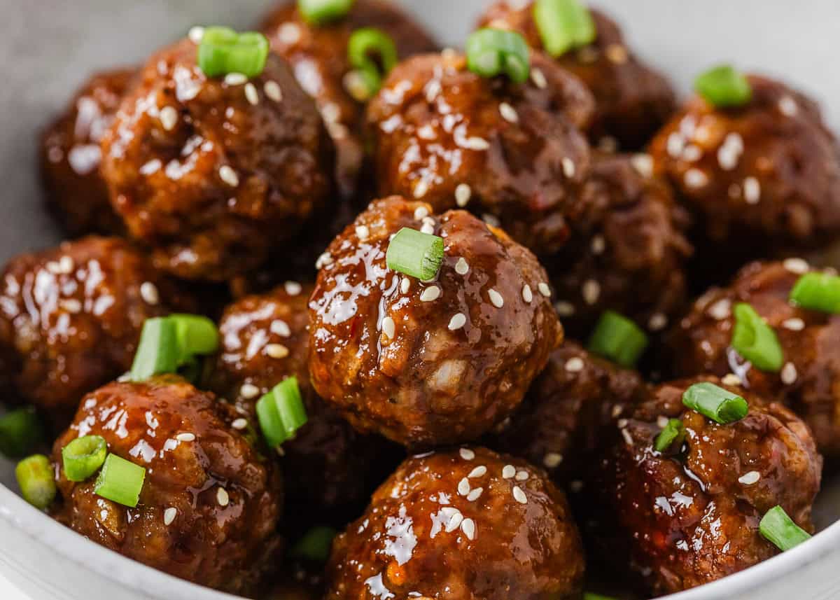 Glossy sticky pork meatballs topped with sesame seeds and sliced green onions.