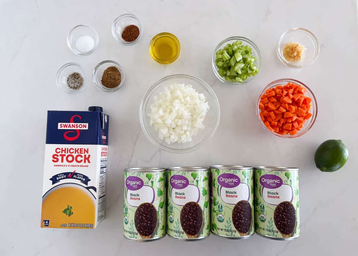 Ingredients for black bean soup including black beans, broth, onion, carrots, celery, garlic, lime, olive oil and spices.