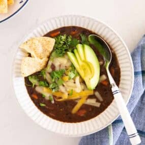 Bowl of black bean soup topped with avocado, cilantro, cheese and tortilla chips.