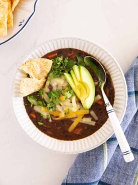 Bowl of black bean soup topped with avocado, cilantro, cheese and tortilla chips.
